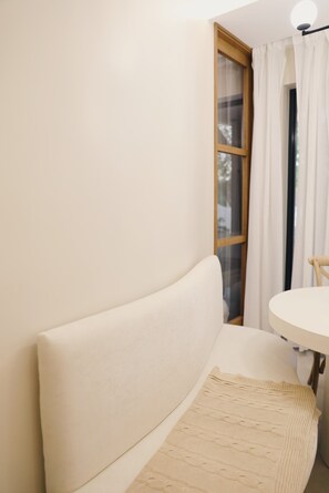 A room with a white sofa, a round table, and a window with curtains.