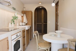 A modern kitchen with a built-in oven, a dining table with chairs, and a wooden cabinet.