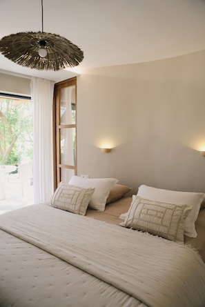 A bedroom with a bed, pillows, a hanging light fixture, and a window with curtains.