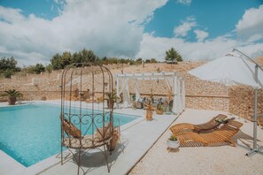 A pool area with a swing chair, lounge chairs, and a pergola with seating.