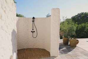 A small, enclosed shower area with a hose and a wooden floor, surrounded by a white wall and potted plants.