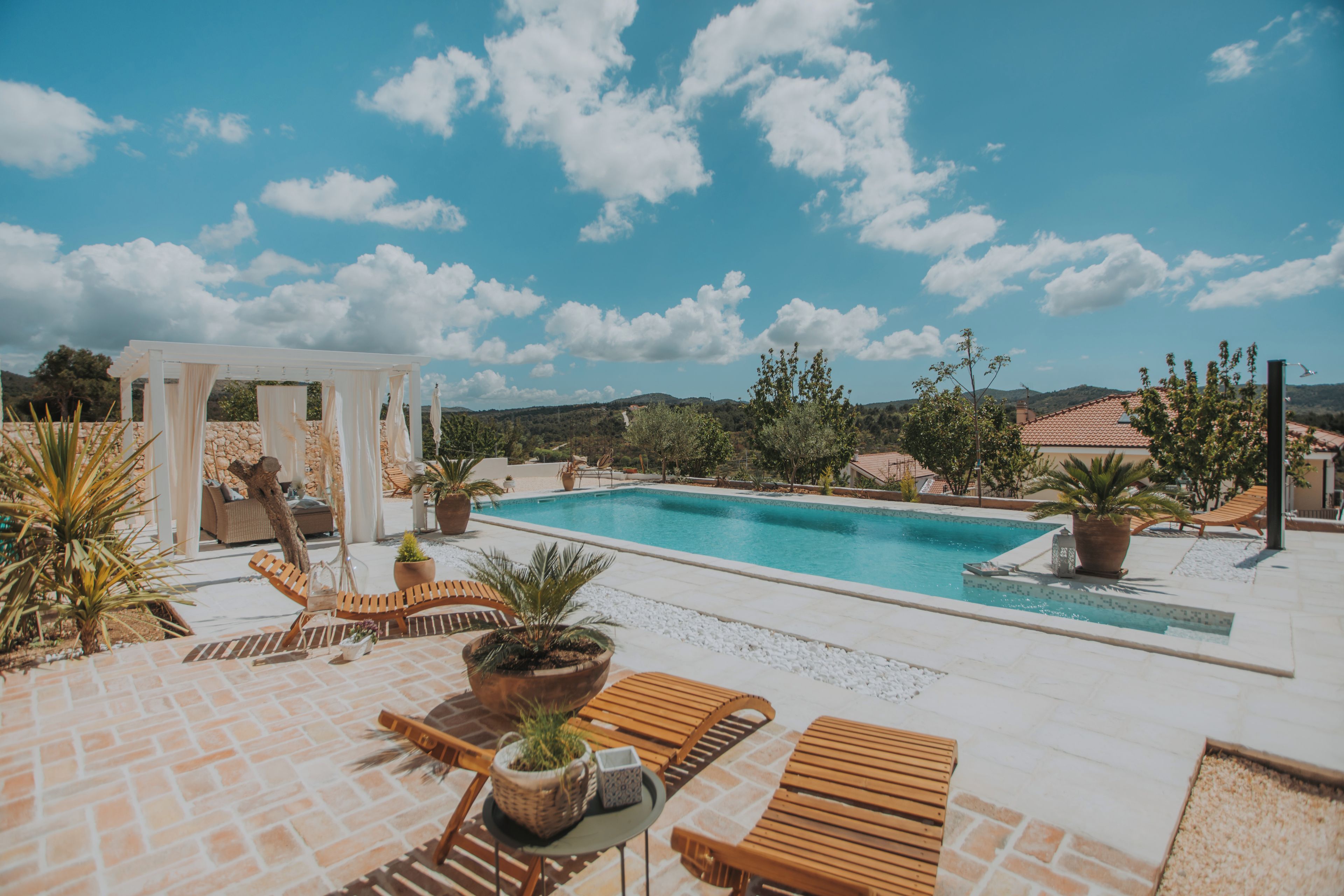 A pool area with a pergola, lounge chairs, and potted plants.