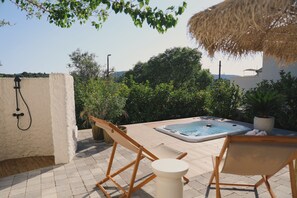 A hot tub with a view of the countryside, surrounded by potted plants and a wooden chair.