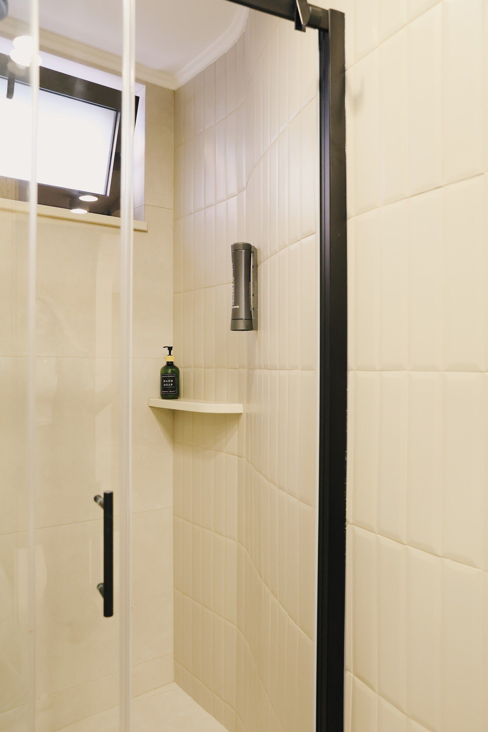 A shower area with a glass door, a hand soap dispenser on a shelf, and a towel rack.