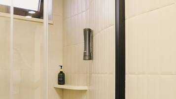 A shower area with a glass door, a hand soap dispenser on a shelf, and a towel rack.
