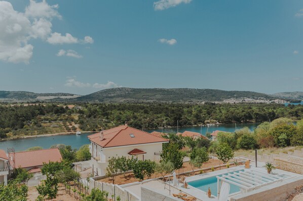 A villa with a swimming pool, surrounded by greenery and a view of a lake.
