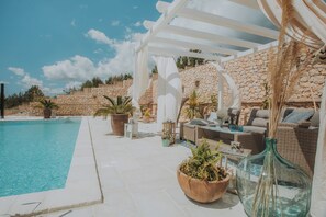 Zona de piscina con muro de piedra, muebles de exterior y plantas en macetas.