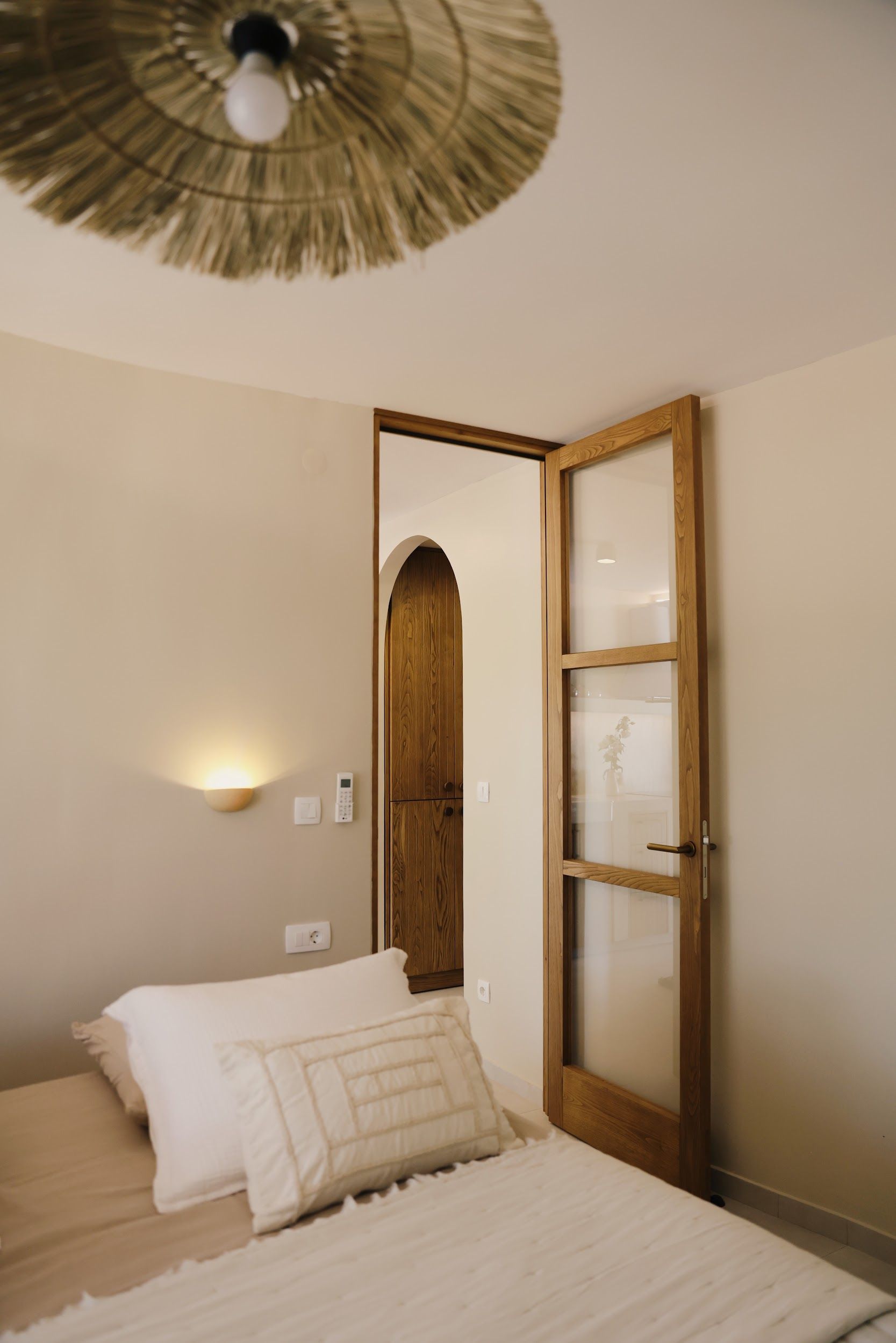 Une chambre à coucher comprenant un lit, une armoire en bois, un luminaire fixé au mur et un ventilateur de plafond.