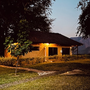 A house with a thatched roof, surrounded by a well-maintained garden and a clear view of the mountains in the background.