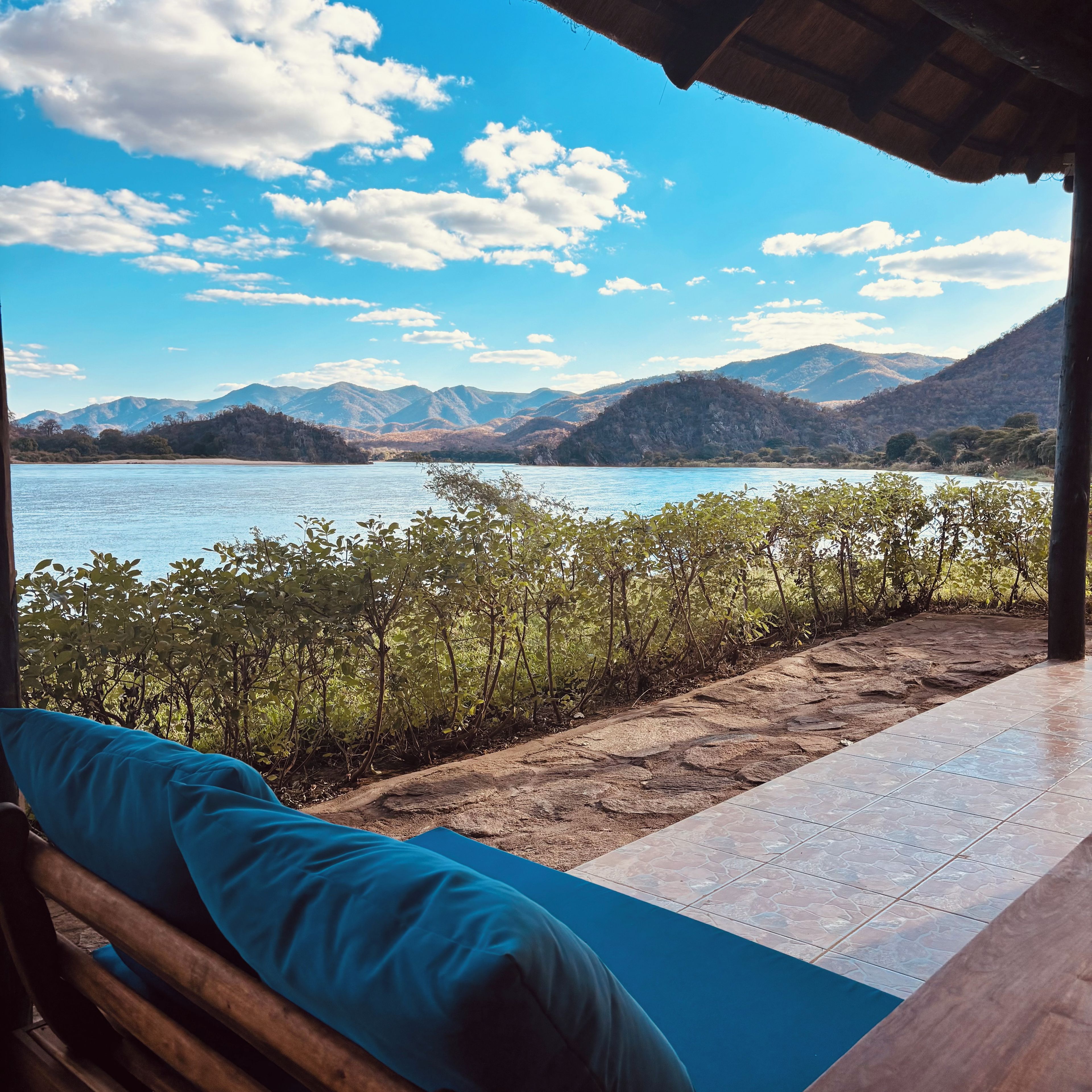Quarto com vista para um lago e montanhas, um banco de madeira e piso de azulejos.