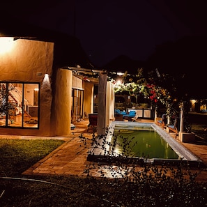 Vista nocturna de una casa moderna con piscina, mobiliario exterior y un patio bien iluminado.