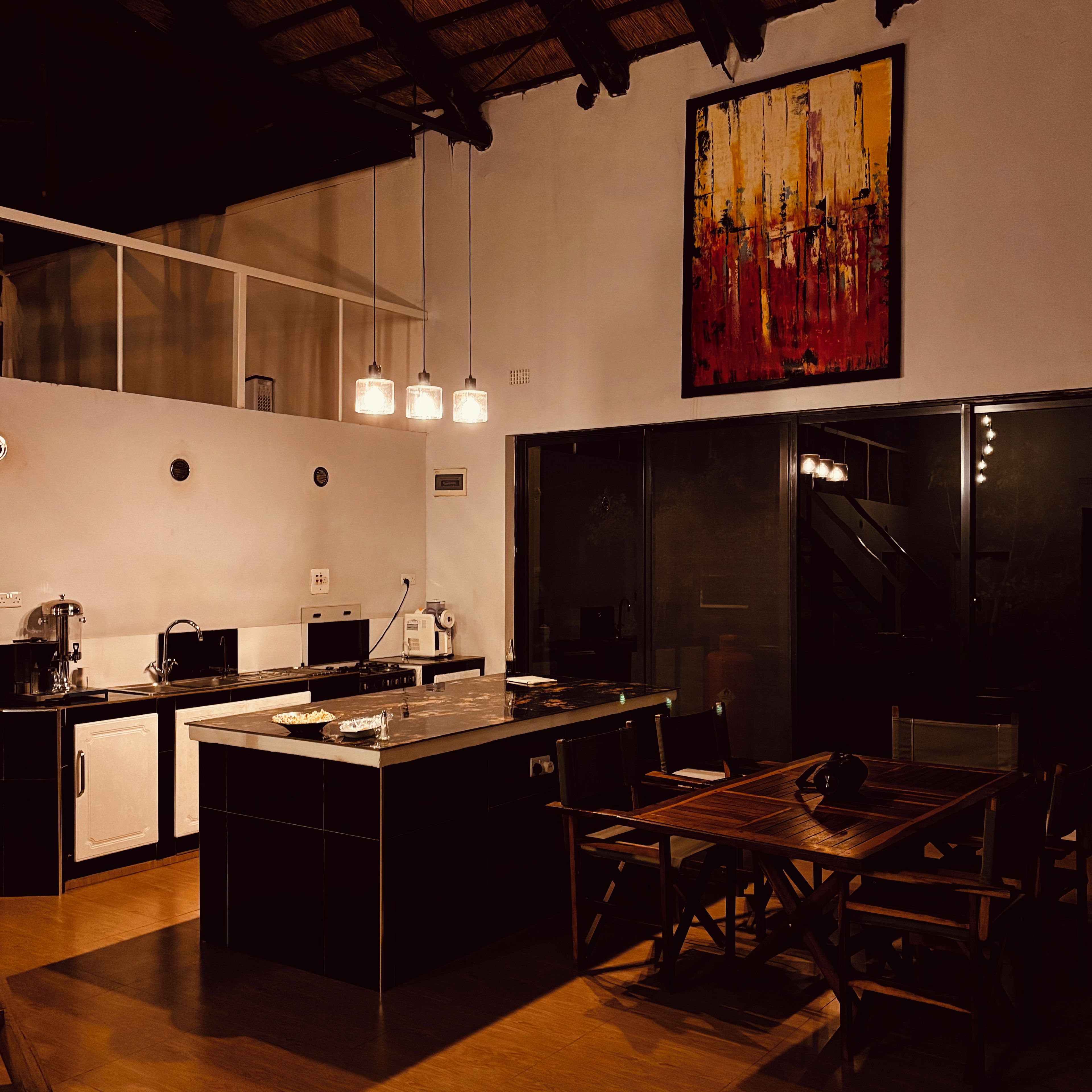 Cozinha moderna com ilha central, iluminação pendente e uma grande pintura na parede.