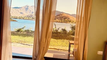 A room with a bed, a view of a lake, and mountains in the distance.