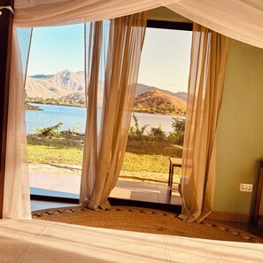 A room with a bed, a view of a lake, and mountains in the distance.