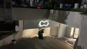 Un bâtiment moderne doté d’un logo original en forme d’infini, d’un petit espace jardin agrémenté de plantes en pot et d’une entrée bien visible.