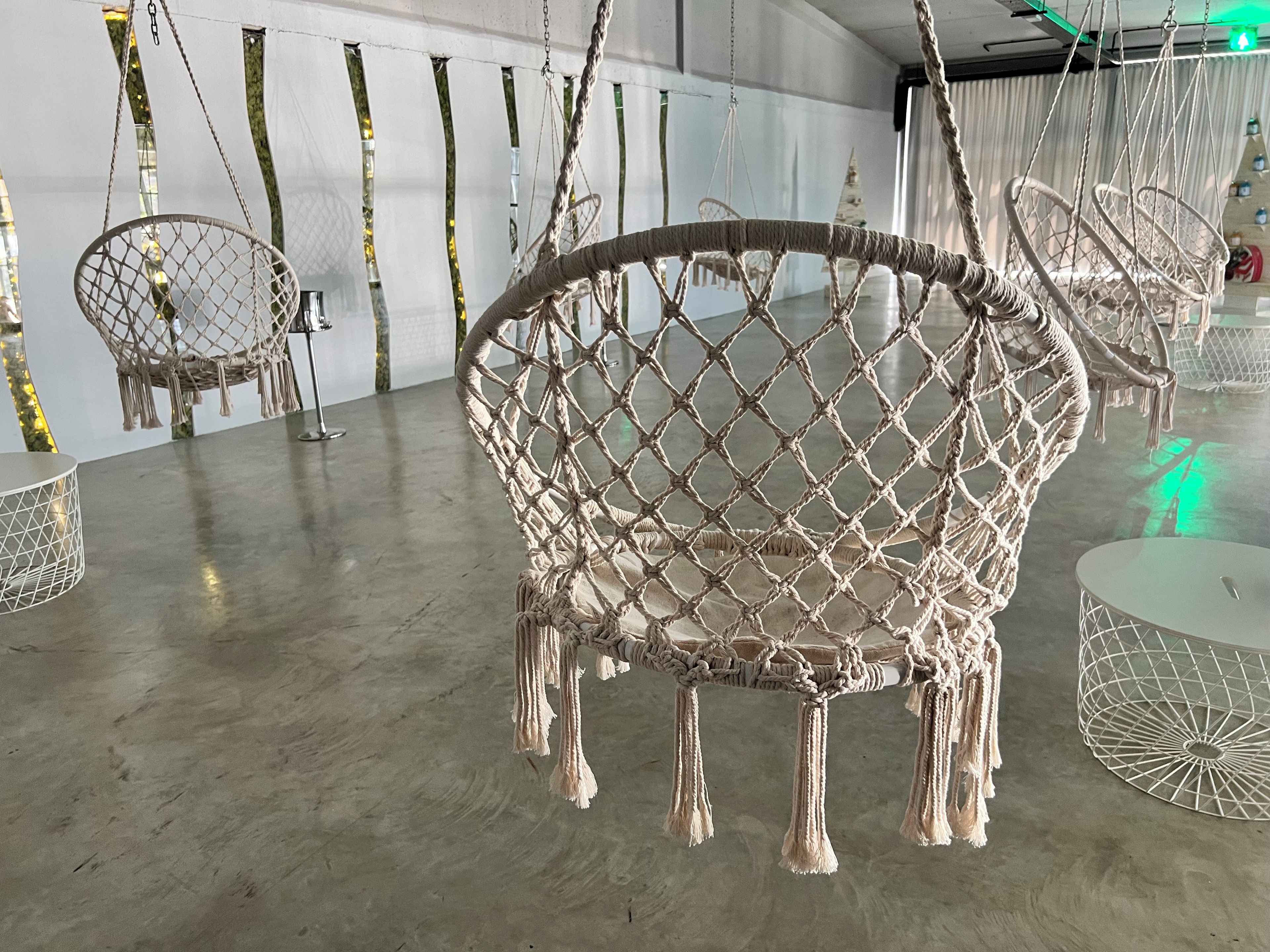 Una stanza con poltrone in macramè, un tavolo rotondo e una sedia sospesa in macramè.