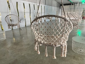 A room with macramé chairs, a round table, and a hanging macramé chair.