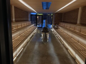Un couloir doté de bancs et d’une colonne centrale, qui mène à une porte en verre.
