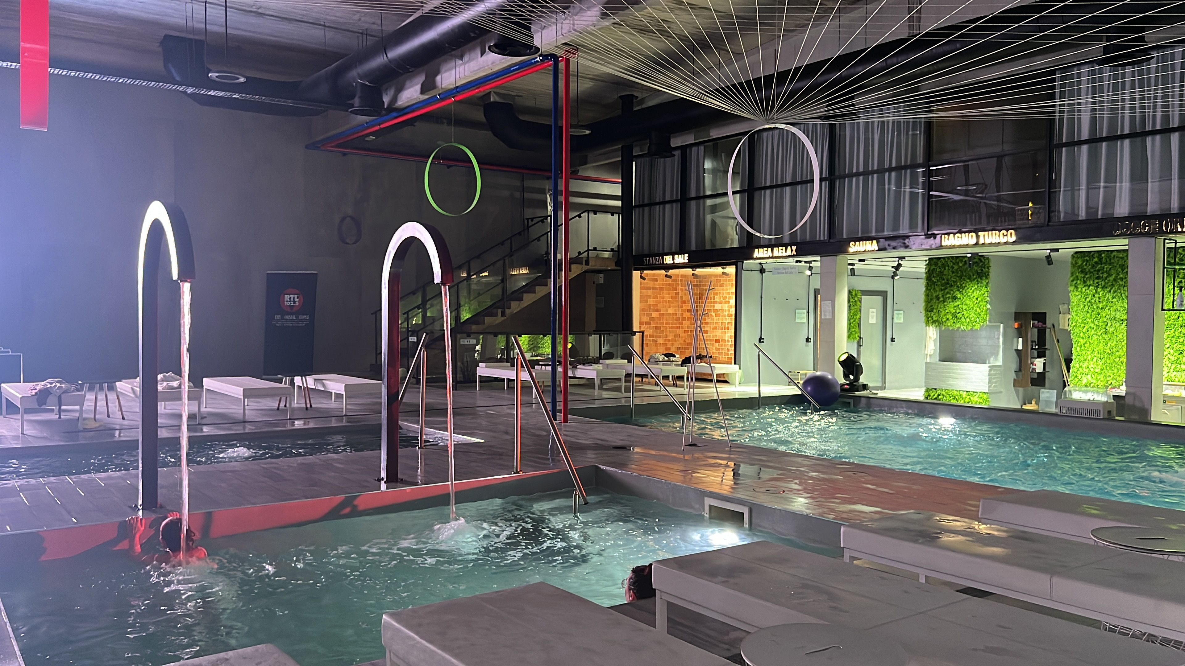 Une piscine intérieure dotée de plusieurs couloirs, un espace sauna et un espace de détente avec des sièges.