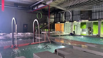 Une piscine intérieure dotée de plusieurs couloirs, un espace sauna et un espace de détente avec des sièges.