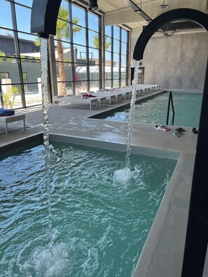 An indoor swimming pool with clear water, benches, and a view of palm trees outside.