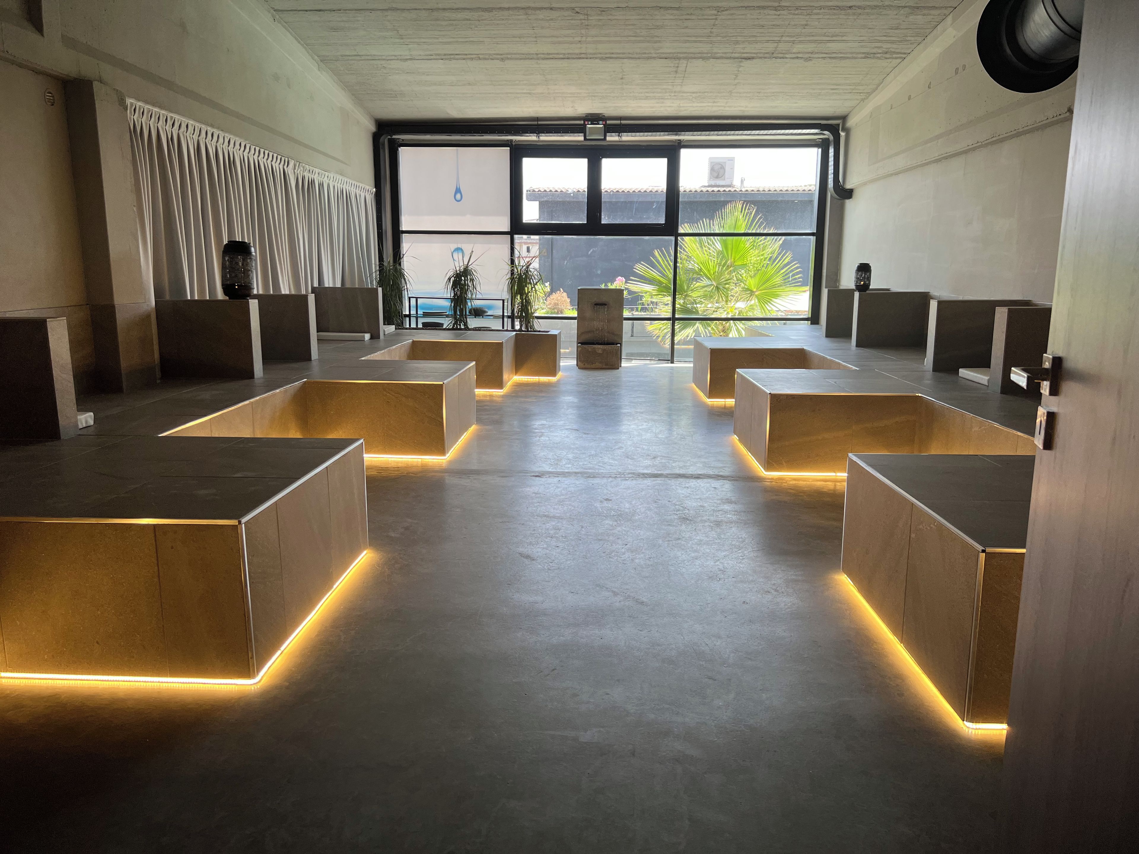 Un interior moderno con una zona de estar central, ventanas amplias y un techo de hormigón.