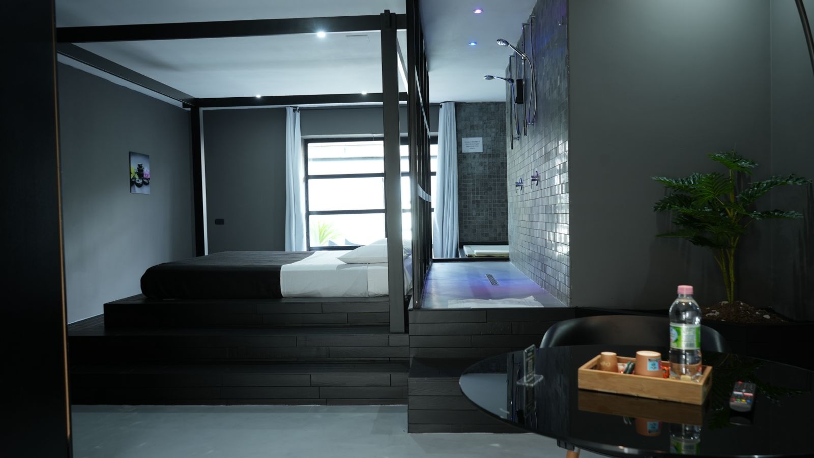 Camera d'albergo moderna con un letto, un tavolino con vassoio, una pianta e vista su un'area benessere.