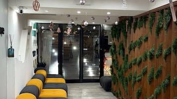 A spa industry reception area with a modern design, including a reception desk, seating area with yellow and gray sofas, and a wooden wall with greenery.