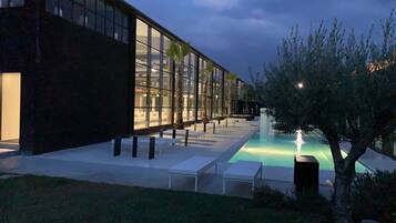 A modern building with a glass facade, a pool, and outdoor seating.