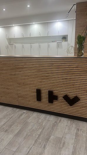 A reception area with a wooden panel wall, a white cabinet with glass doors, and a plant on the right. - ITV CASERTA (San Nicola La Strada)