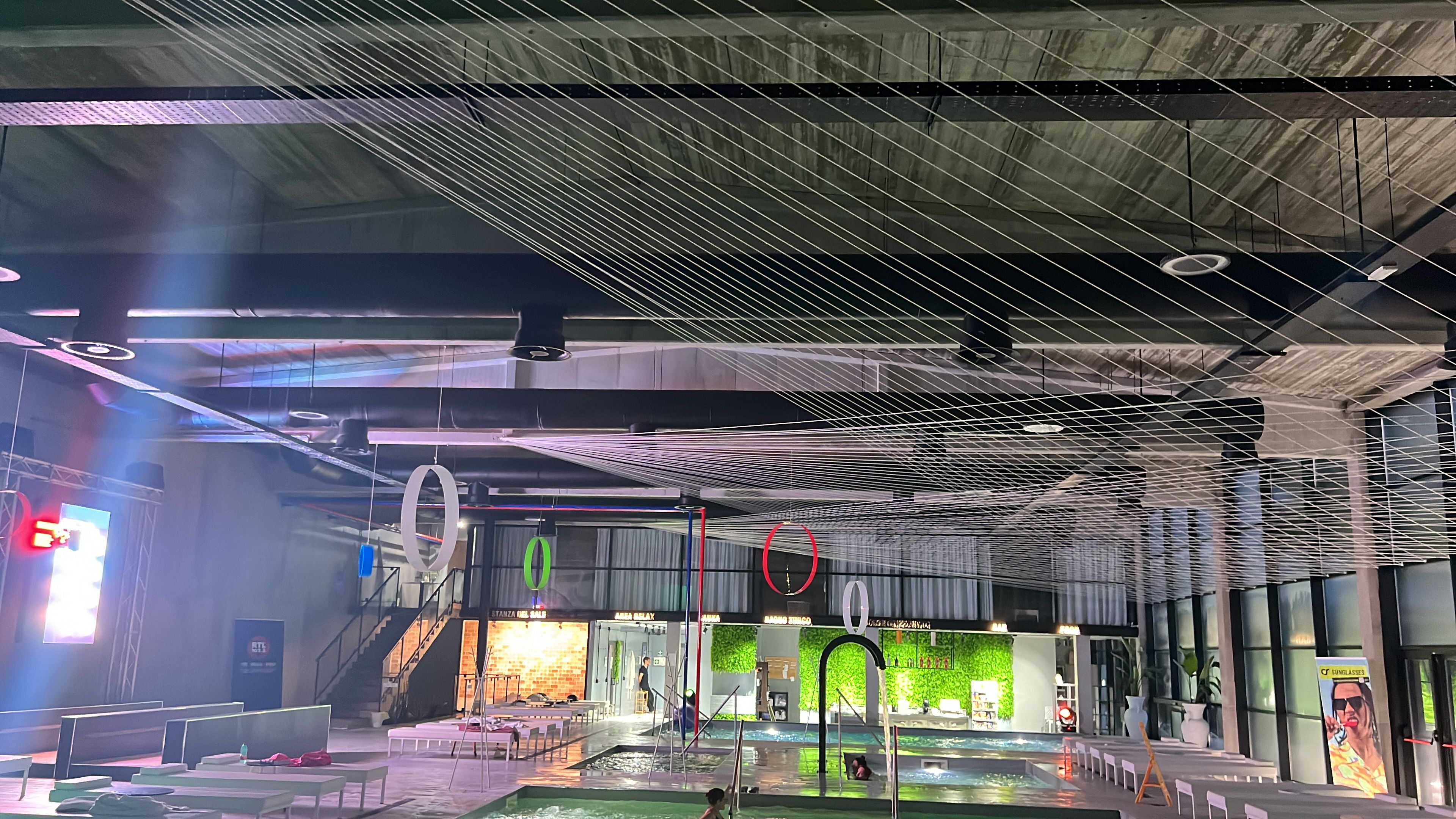 Un espace piscine intérieure au design moderne, comprenant un plafond doté de luminaires linéaires et un escalier apparent menant à un niveau supérieur.