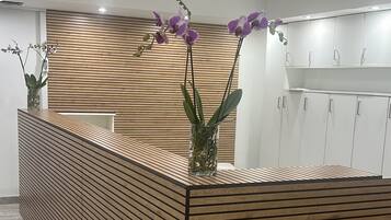 Un comptoir d'accueil avec un design composé de lattes de bois, un vase contenant des orchidées violettes et, au fond, un espace cuisine moderne.
