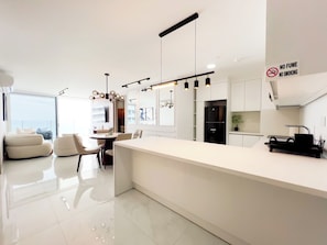 A modern kitchen with a white countertop, black appliances, and a dining area with a white sofa and chairs.