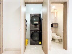Et lille badeværelse med toilet, vaskemaskine og en hylde.