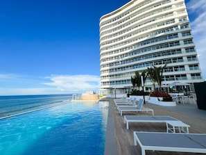 A hotel with a poolside area, a clear view of the ocean, and a multi-story building with balconies.