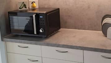 Eine Küche mit weißen Schränken, einer Mikrowelle auf der Arbeitsfläche und einer kleinen Obstauslage.