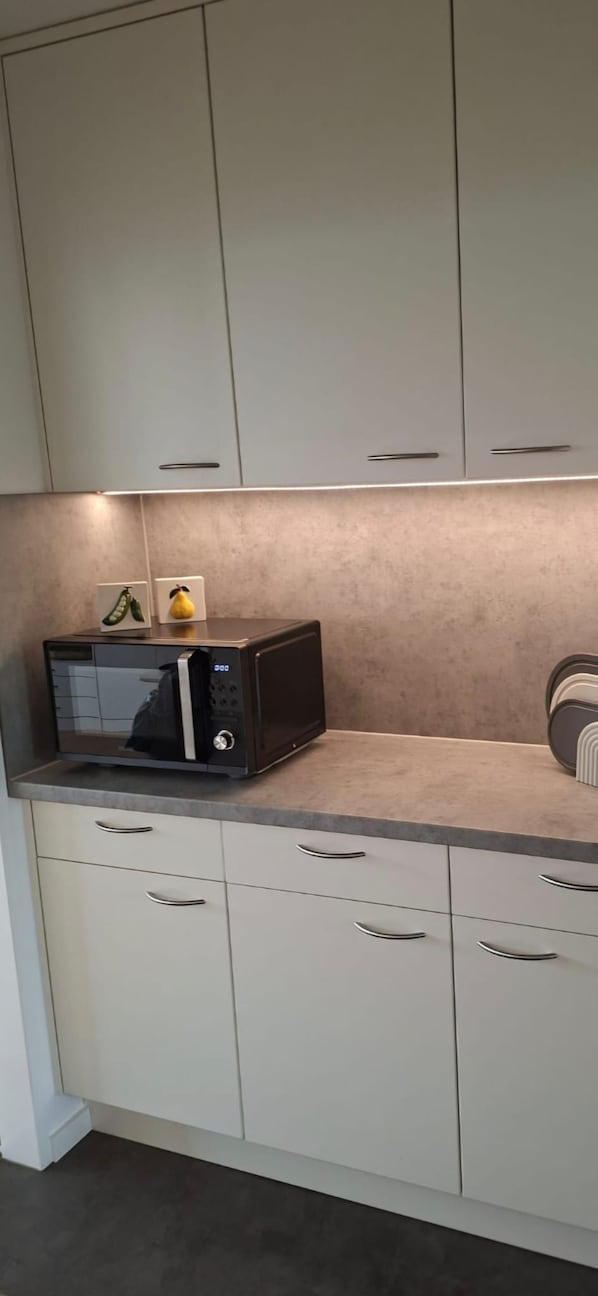 A kitchen with white cabinets, a microwave on the countertop, and a small fruit display.