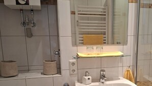 Et moderne badeværelse med toilet, vask og bruser. Der er håndklæder og en skraldespand.
