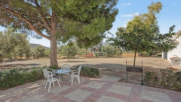 Un patio exterior con una mesa y sillas, rodeado de árboles y un cielo despejado.