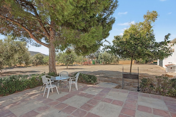 Une terrasse extérieure avec une table et des chaises, entourée d’arbres et sous un ciel dégagé.