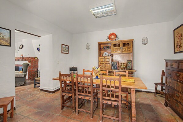 Un comedor con mesa y sillas de madera, una zona de cocina con armarios y estufa, y piso de baldosas.