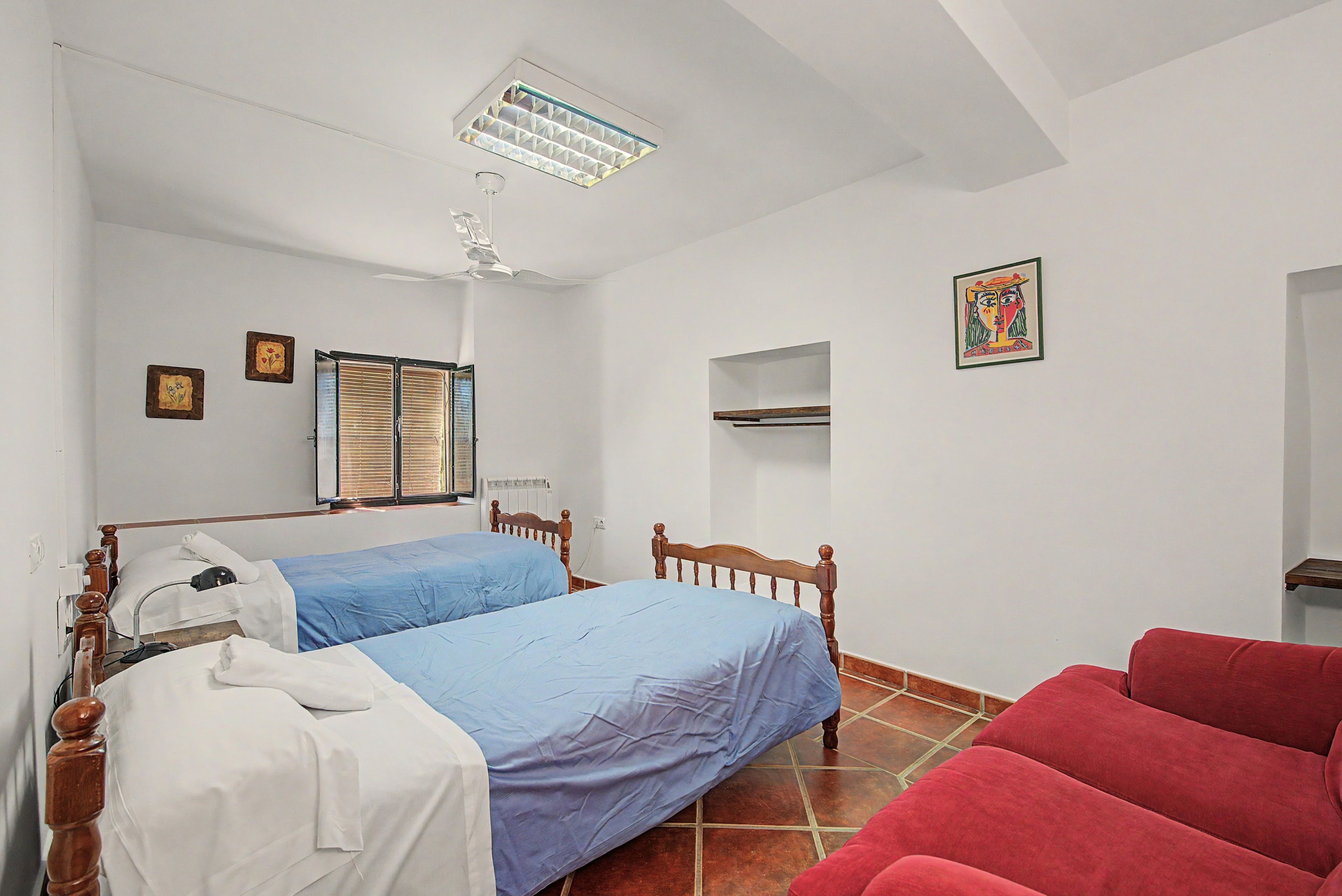 Un dormitorio con dos camas, una silla roja, un radiador y una lámpara en el techo.