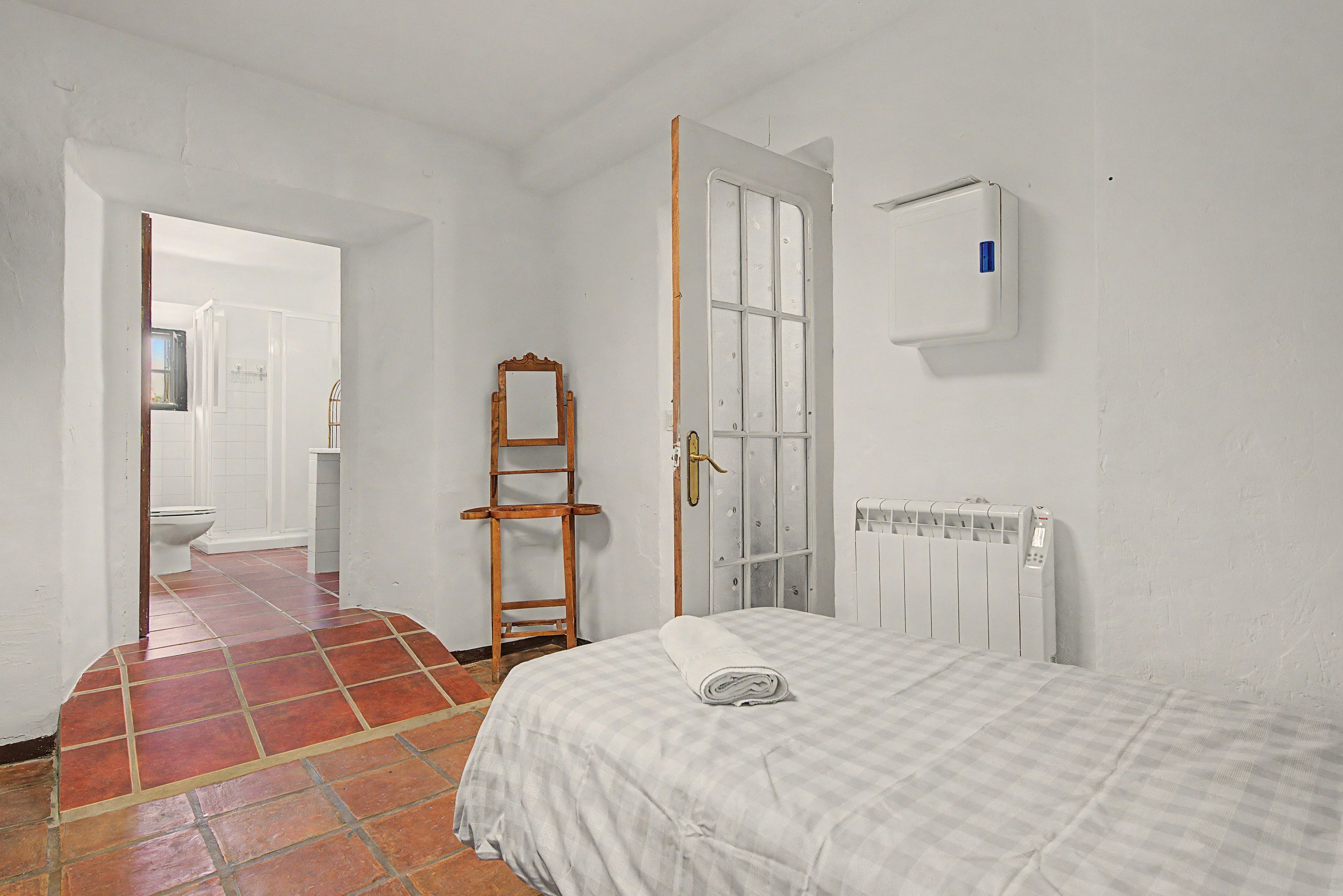 Una camera da letto con un letto, un termosifone, una scala in legno e una porta che dà su un bagno.