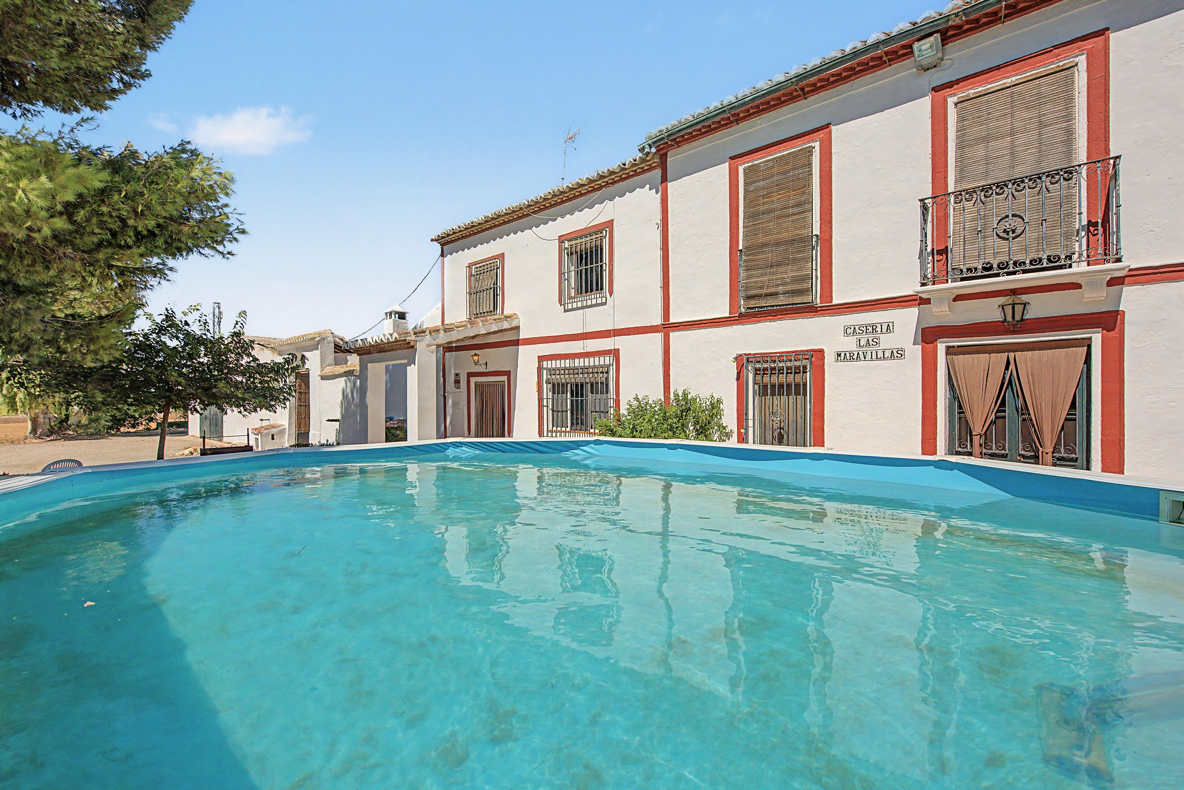 A building with a swimming pool, multiple windows with bars, and a sign that reads 'CASERIA LAS MARAVILLAS'.