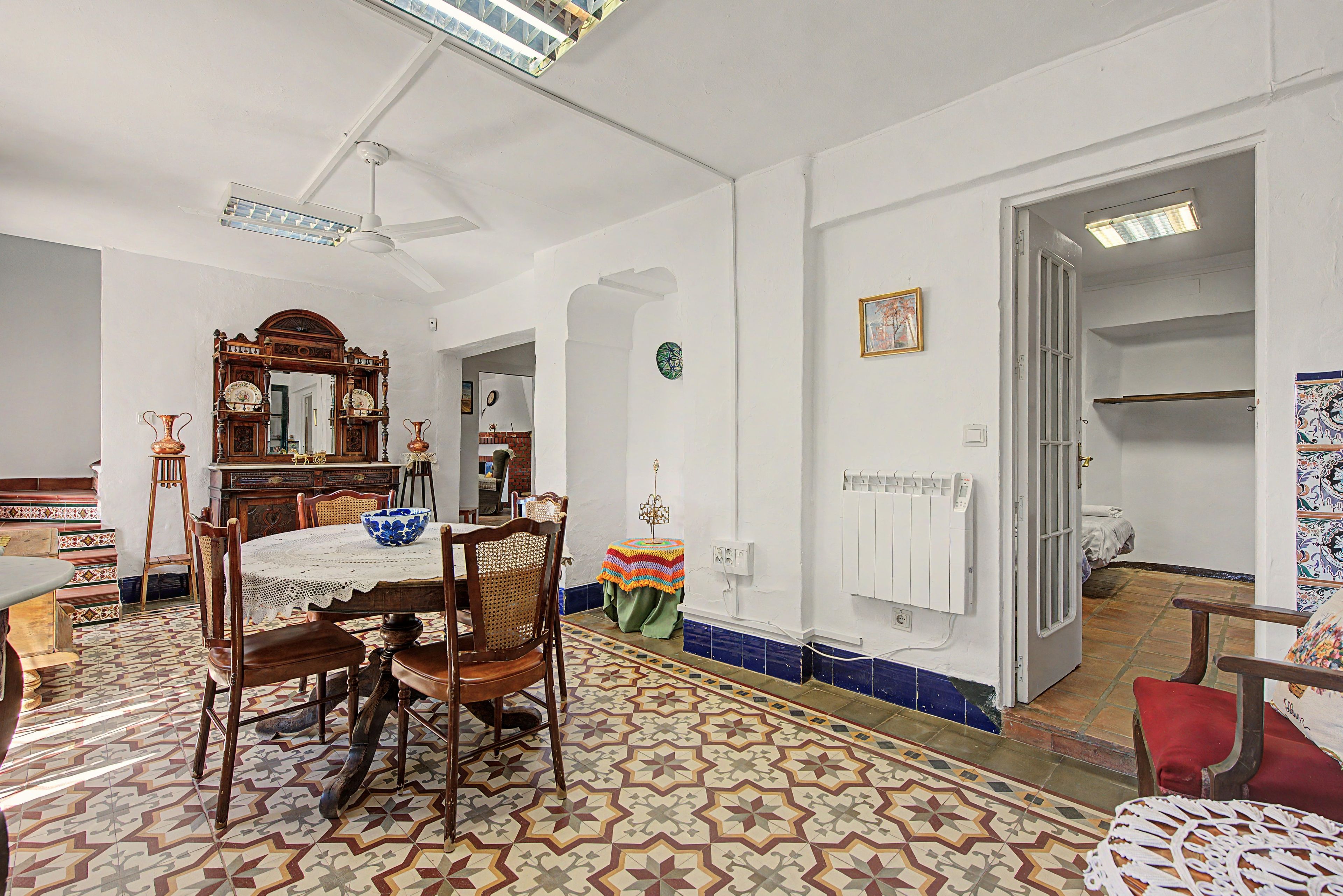 Uma sala de jantar com uma mesa redonda, cadeiras e piso estampado. Há um espelho sobre a mesa e um radiador na parede.