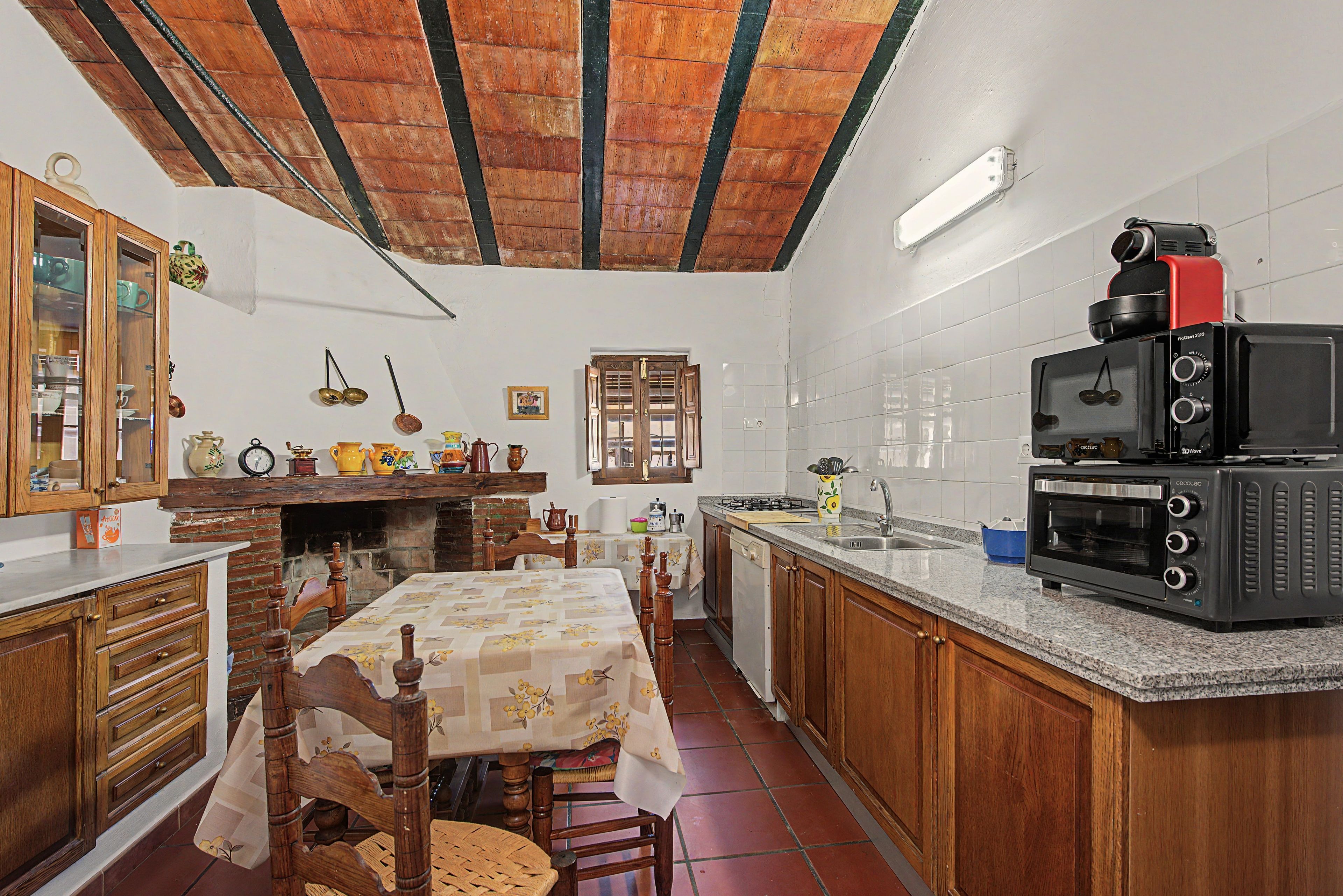 Una cocina con armarios de madera, una mesa de comedor con mantel floreado, una estufa integrada y un microondas.