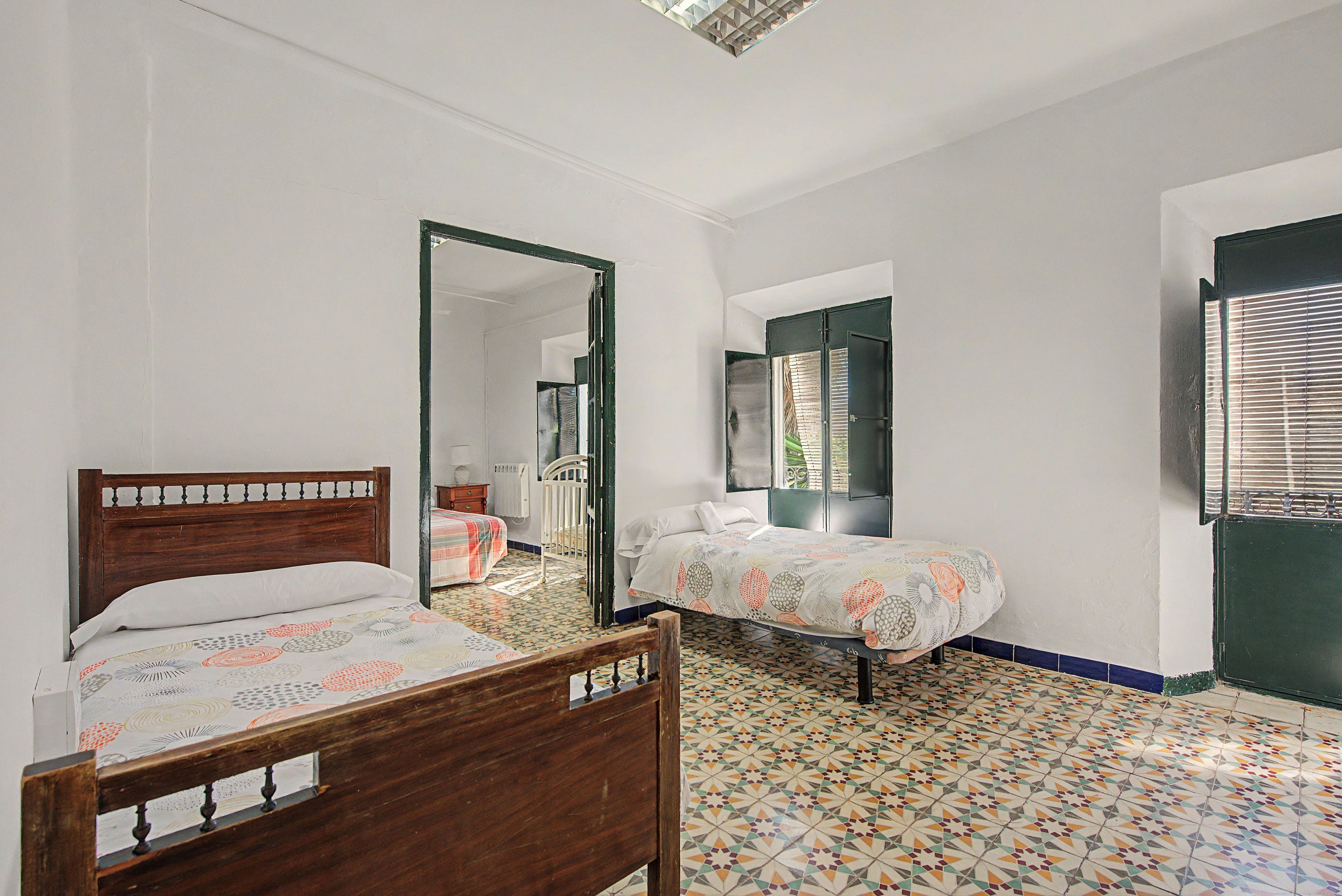 A bedroom with a wooden bed, a bedside table, a chair, a mirror, and a window with blinds.