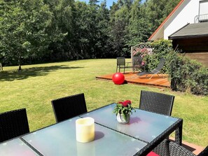 A patio with a glass table, chairs, a red ball, and a wooden deck. - 11a/t6 Holiday Home Park \"freesenbruch\" (Zingst)