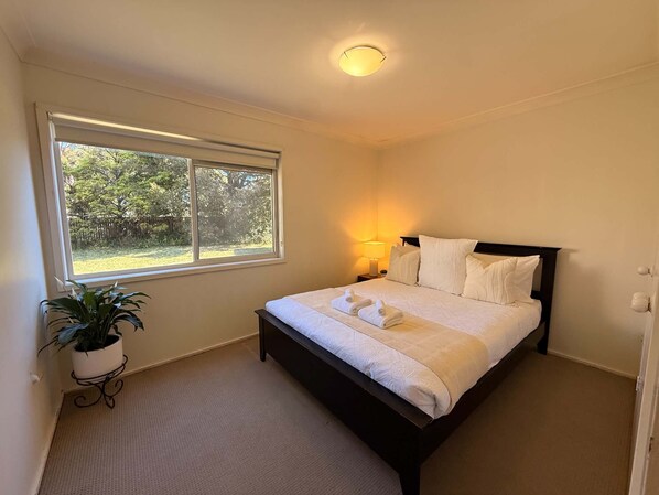 A bedroom with a large window, a bed, a bedside lamp, and a potted plant.