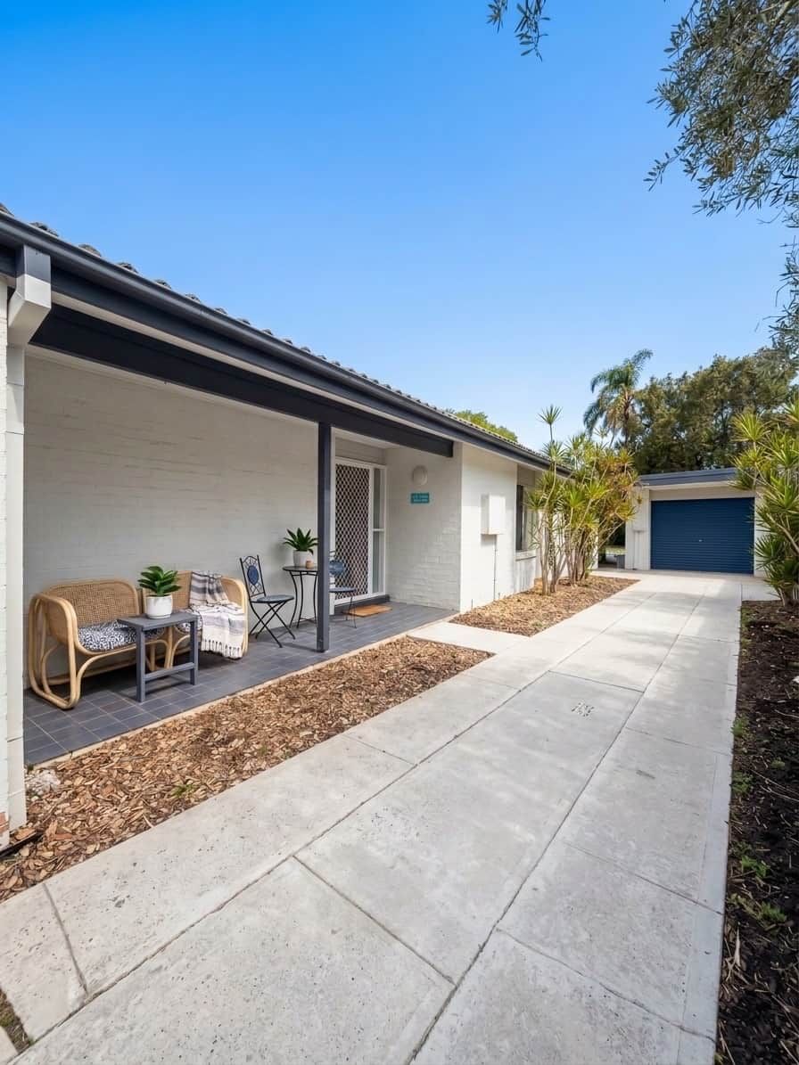 Ein Wohnhaus mit überdachter Veranda, Sitzgelegenheit im Freien und einer Garage.